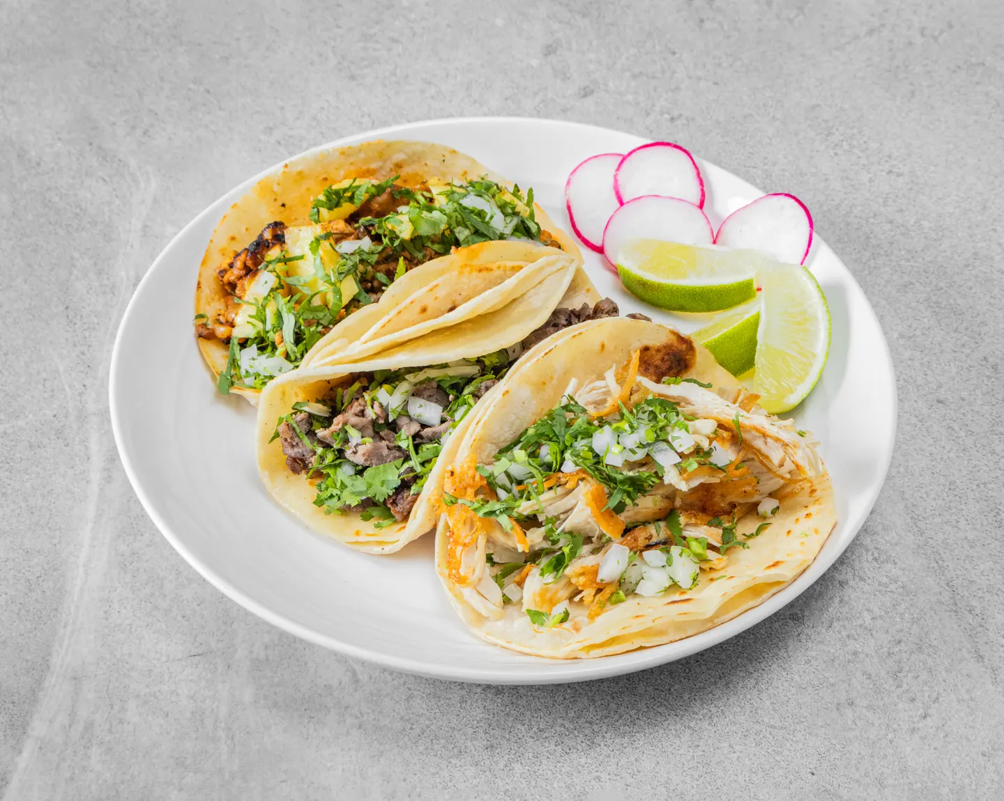 Tres tacos con cilantro y cebolla, servidos con rábano y limón